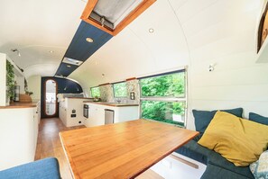 Cozinha compacta com ilha central, área de jantar com mesa de madeira e sofá com almofadas.