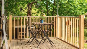 Una terraza de madera con una mesa y sillas, rodeada por una valla de madera y árboles.