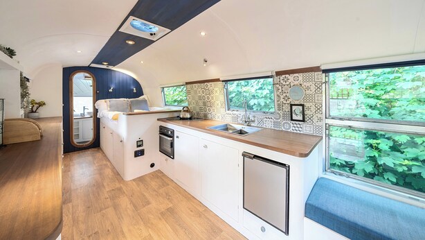 Una cocina compacta con horno integrado, lavamanos y ventana con vistas a la vegetación.