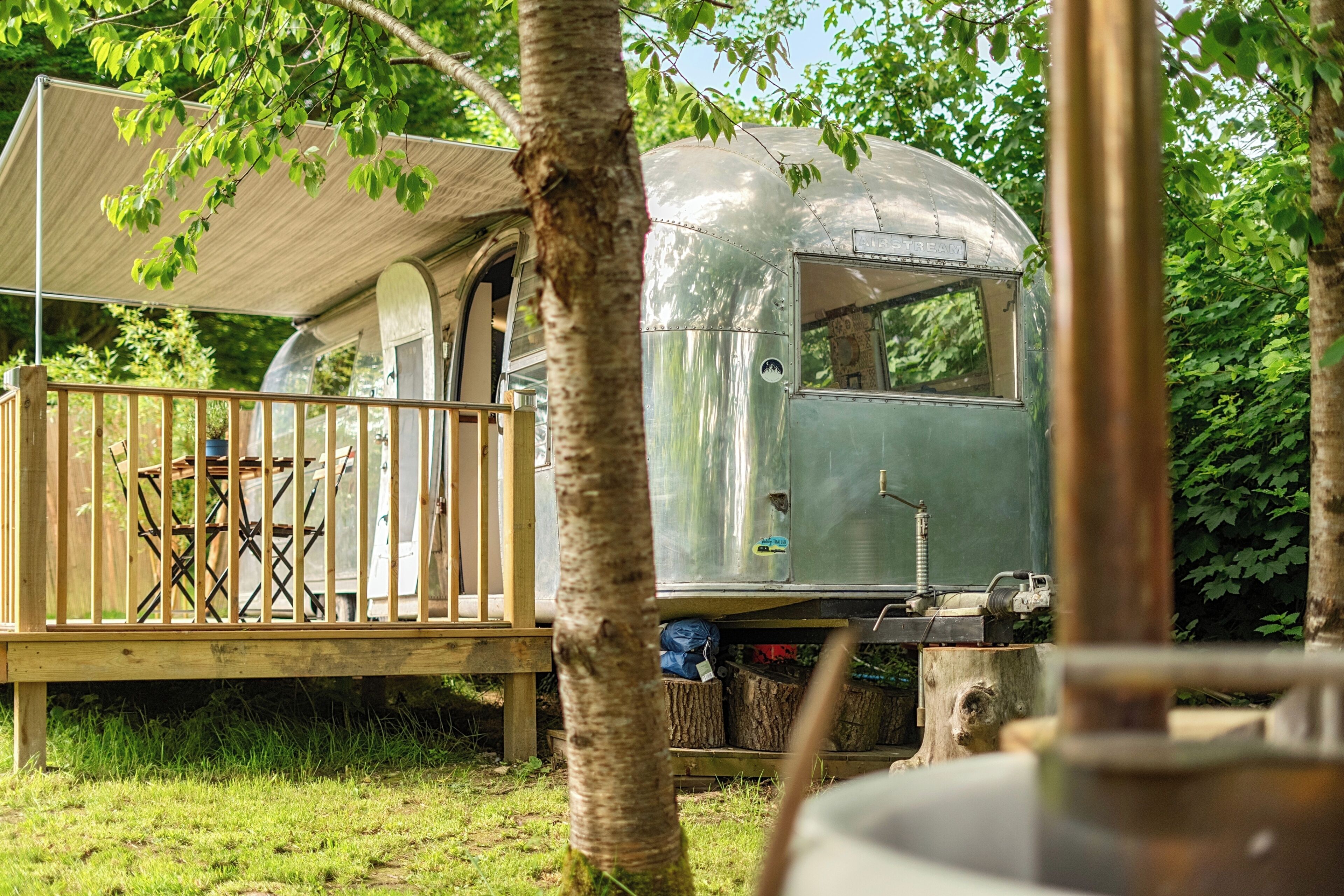 Een vintage caravan met een overdekt terras, een tafeltje en een stoel.