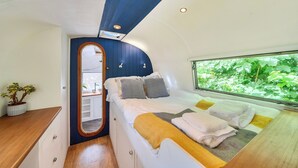 Un dormitorio acogedor con cama, mesita de noche, espejo y ventana con vistas a la vegetación.