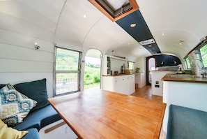 A compact living space with a dining area, kitchenette, and a large window offering a view of greenery. - Sleeps 2 - Private Hot Tub - Fire Pit (Cardigan)