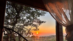 Een kamer met een groot raam dat uitkijkt over een landschap met een zonsondergang.