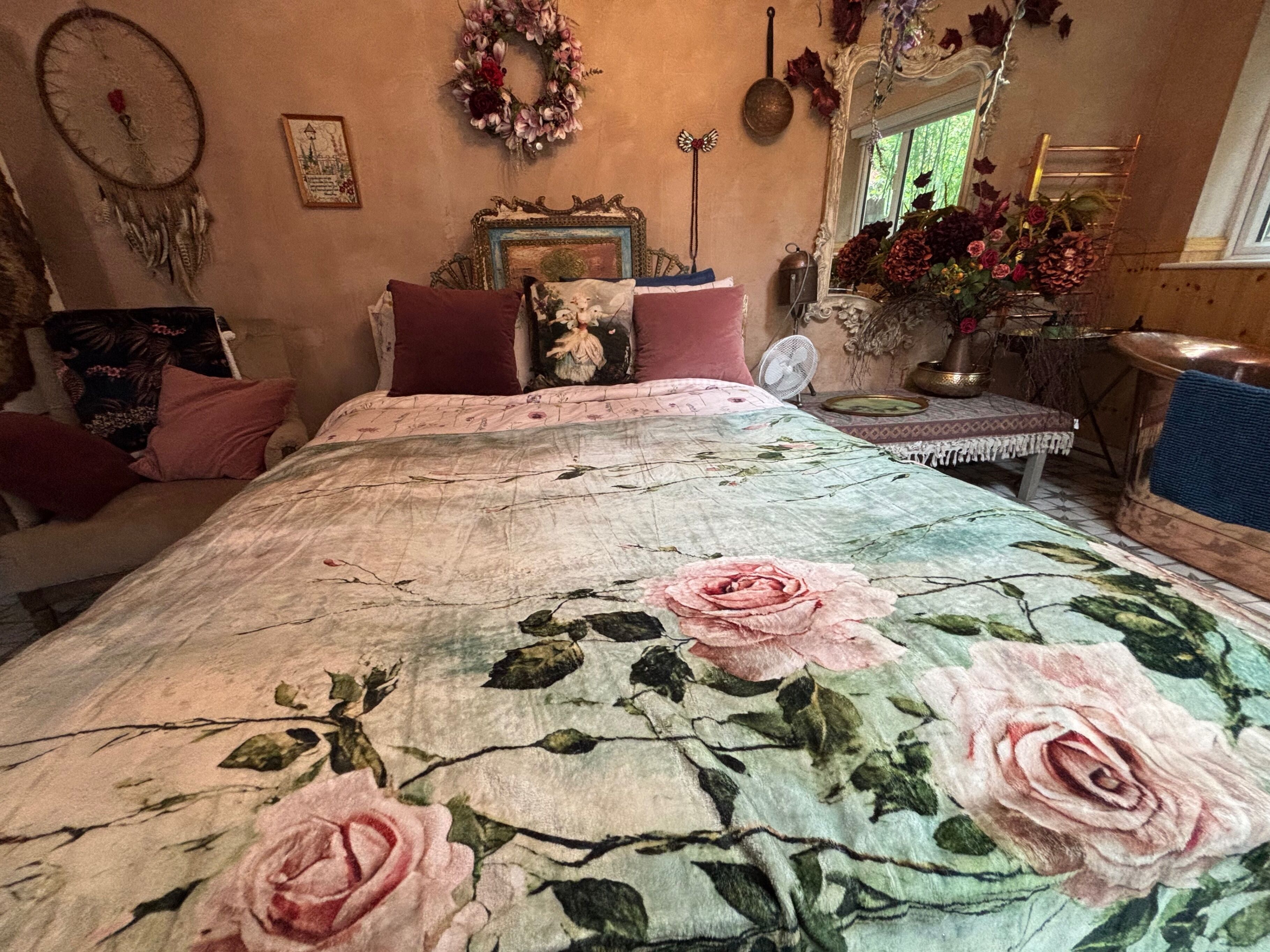 Quarto com colcha florida, penteadeira, espelho e janela com vista para áreas verdes.
