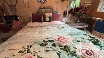 Quarto com colcha florida, penteadeira, espelho e janela com vista para áreas verdes.