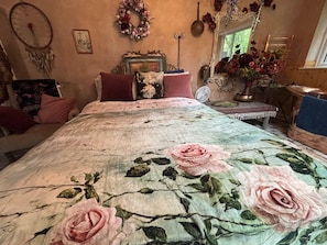 Un dormitorio con colcha estampada, cómoda, espejo y ventana con vista a vegetación.