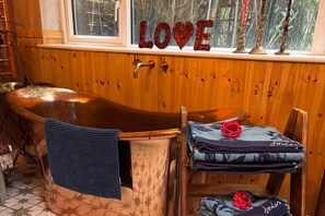 Ein Holzblockhaus-Interieur mit einer Badewanne, einem Fenster mit Blick auf Bäume und einem 'LOVE'-Schild auf der Fensterbank.