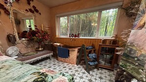 Een kamer met een grote spiegel, een raam met uitzicht op groen, een houten kast en een bed met een bloemenbedekking.