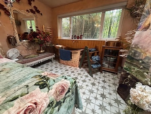 A room with a large mirror, a window with a view of greenery, a wooden cabinet, and a bed with a floral bedspread. - Coastal Cabin / 2 rooms / Sleeps 3 (Liverpool)