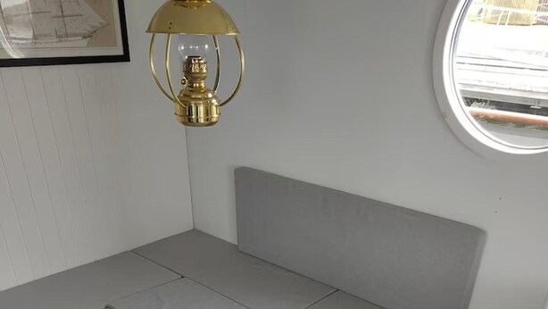 A compact bed with a grey mattress and a headboard, positioned against a white wall with a framed picture above it.