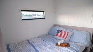 A single bed with a patterned bedspread, a pillow with an American flag design, and a tray with a cup and pastries.