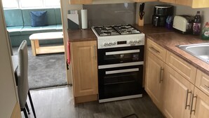 Uma cozinha compacta com fogão a gás, forno e torradeira. Na área de estar adjacente, há um banco e um sofá.