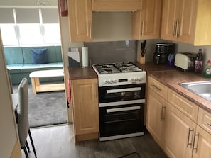 Una cocina compacta con estufa a gas, horno y tostadora. En el área de estar contigua, hay un banco y un sofá.
