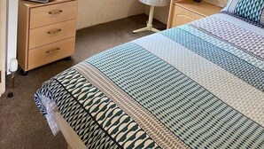 Um quarto com cama, escrivaninha, cadeira, televisão e janela com cortinas.