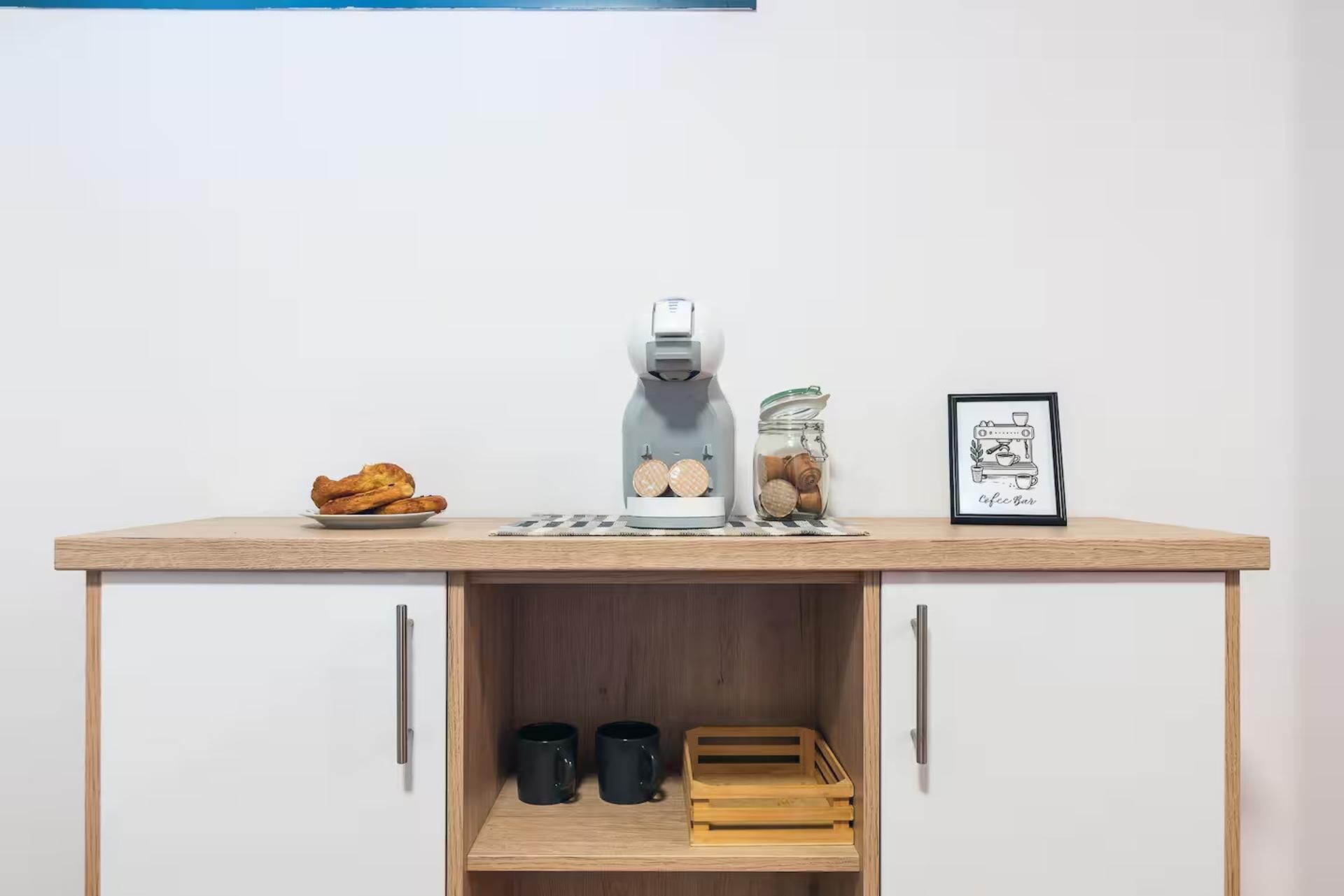 A kitchenette with a coffee maker, a jar of cookies, and a framed picture on the counter.
