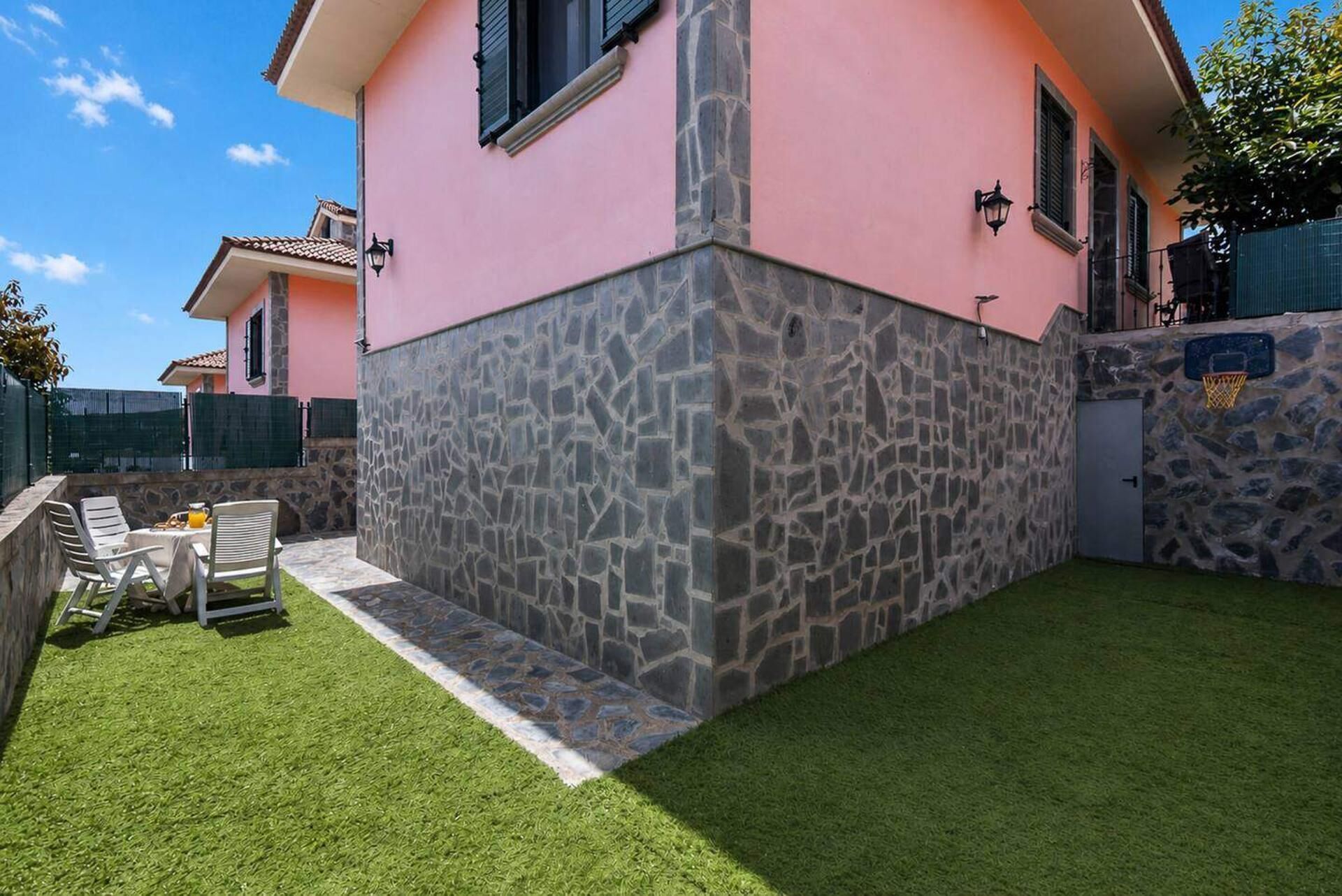 Uma casa com fachada de pedra, um pequeno pátio com mesa e cadeiras, e um gramado bem cuidado.