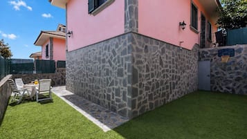 Uma casa com fachada de pedra, um pequeno pátio com mesa e cadeiras, e um gramado bem cuidado.