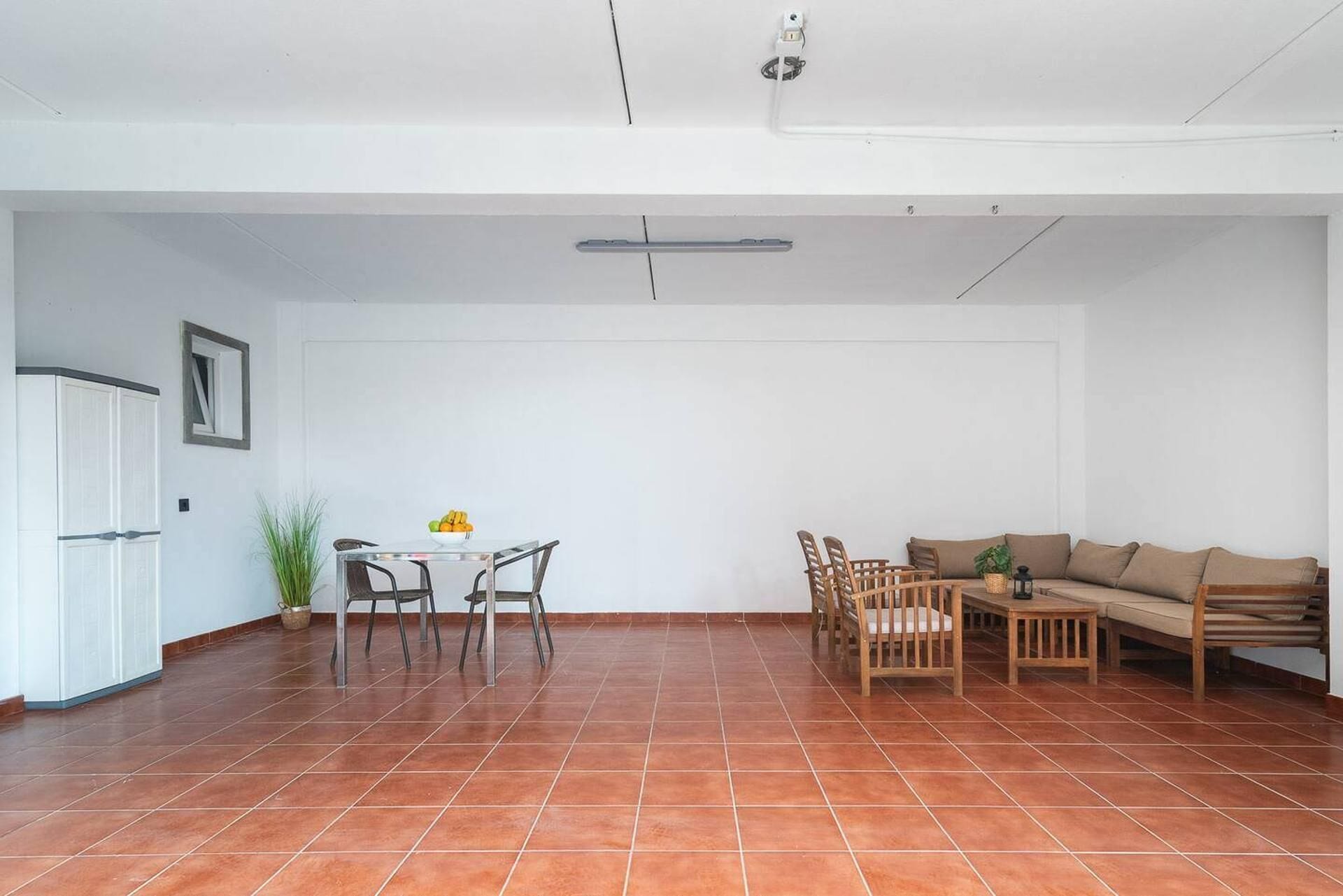 Um quarto amplo com piso de azulejos, uma mesa de jantar com cadeiras, um sofá e uma pequena mesa com uma planta.
