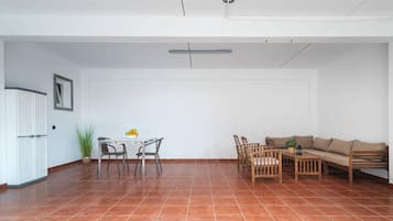 Um quarto amplo com piso de azulejos, uma mesa de jantar com cadeiras, um sofá e uma pequena mesa com uma planta.