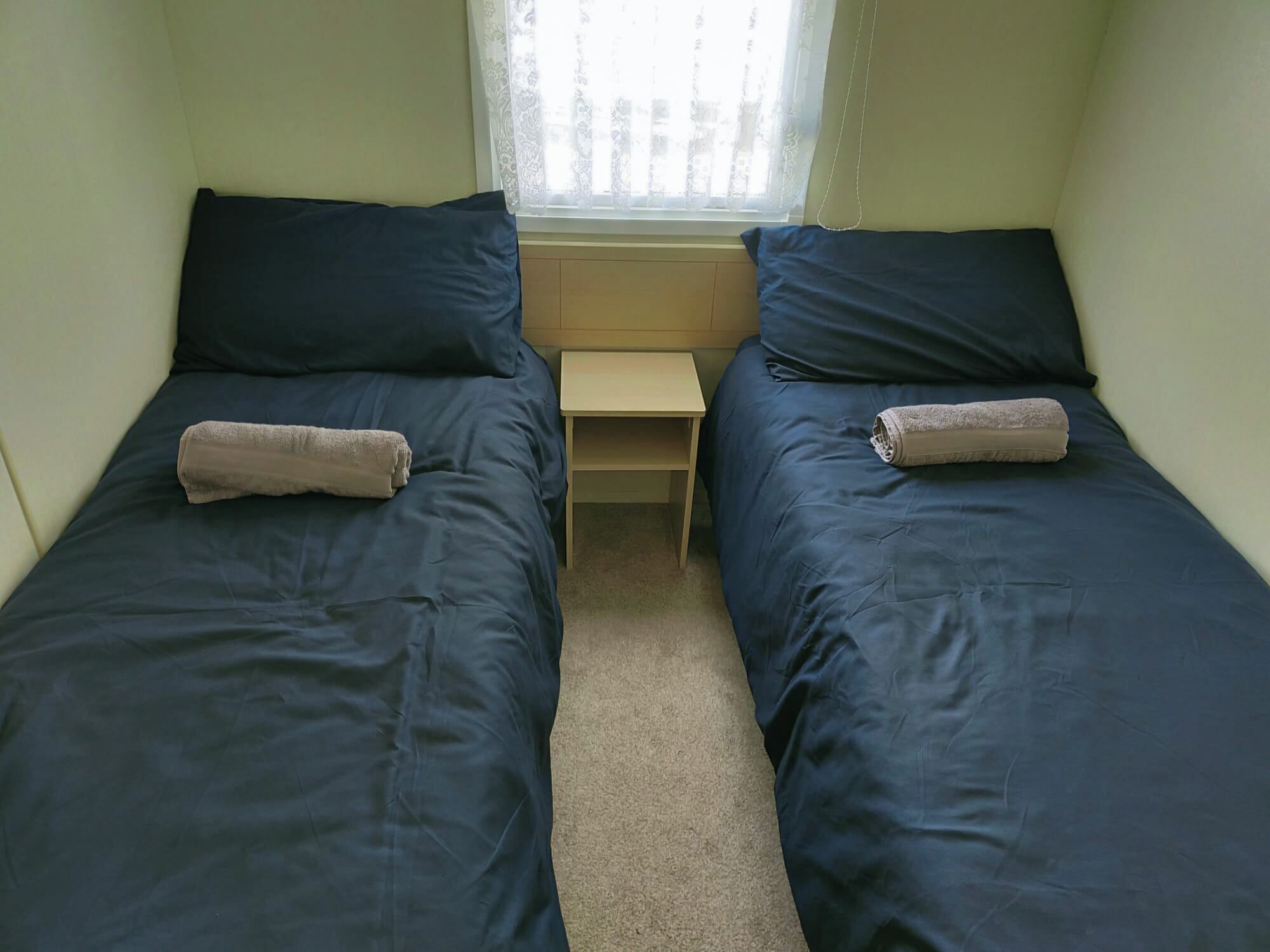 A twin room with two single beds, a nightstand, and a window with sheer curtains.