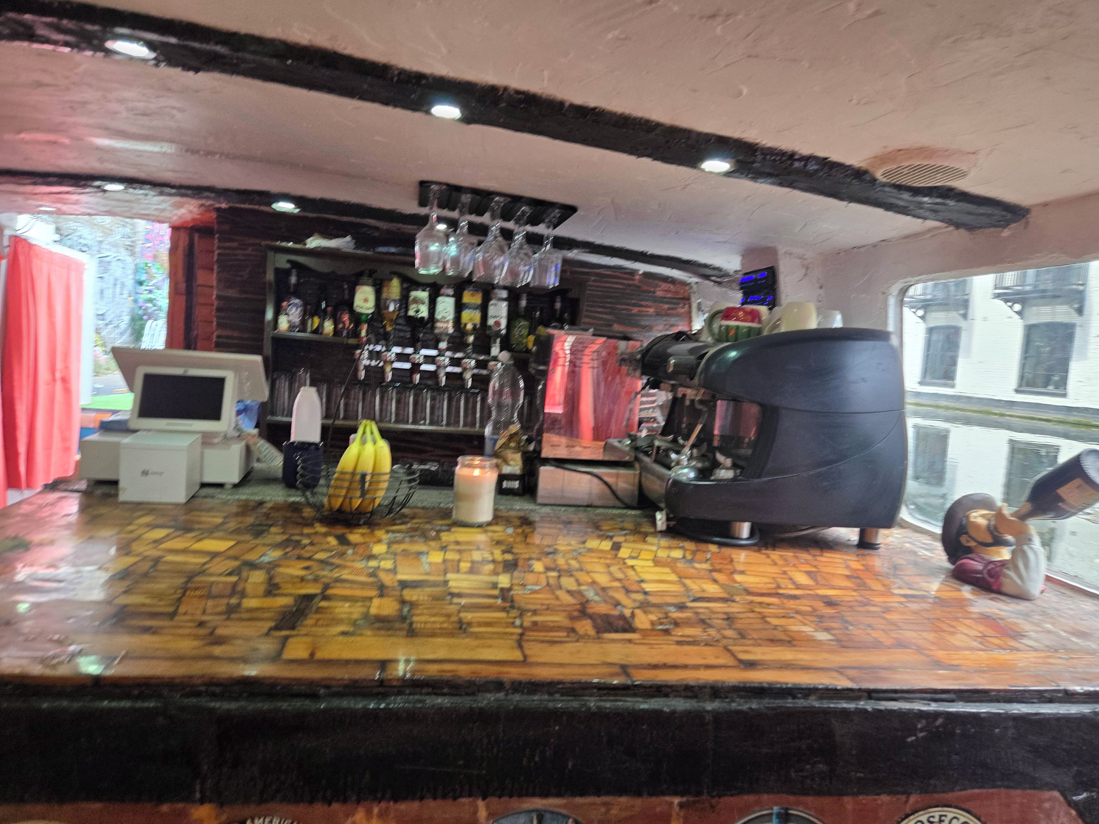 Una zona de bar con una máquina de café, una computadora y varias botellas en estantes.