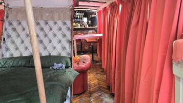 A room with a bunk bed, a small table with chairs, a bar area, and red curtains.