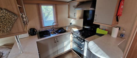 A compact kitchen with a stove, oven, sink, and wooden cabinets.
