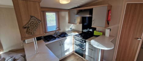 A compact kitchen with a stove, oven, and sink, wooden cabinets, and a window with blinds.