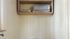 Un bagno con un water bianco, uno scaffale di legno con articoli da toilette e un lavandino bianco.