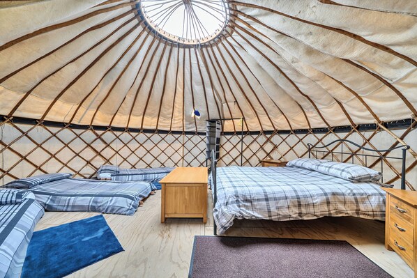 Interior de una yurtas con una cama, muebles de madera y un poste central.