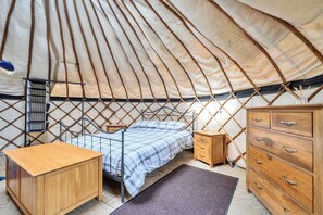 A cozy interior of a round tent with a bed, wooden dresser, and a small shelf. - Yurt Sleeps 5 - Dogs Welcome - Bbq (Bodmin)