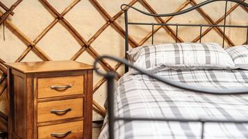 Ein Bett mit Metallgestell und karierter Tagesdecke, ein Nachttisch aus Holz mit Schubladen und eine Wand mit Bambusmuster.