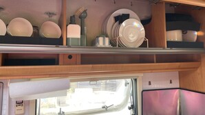 Uma área de cozinha com prateleiras contendo pratos e tigelas, uma janela com vista e um painel de controle para um aparelho.