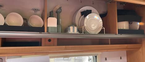 A kitchen area with shelves holding plates and bowls, a window with a view, and a control panel for a device.