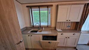 Una kitchenette compacta con pileta, una ventana con persianas, horno integrado y un armario.