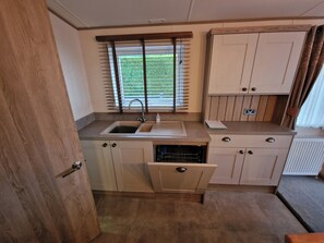 Eine kompakte Küchenzeile mit Spüle, einem Fenster mit Jalousien, einem Einbauofen und einem Schrank.