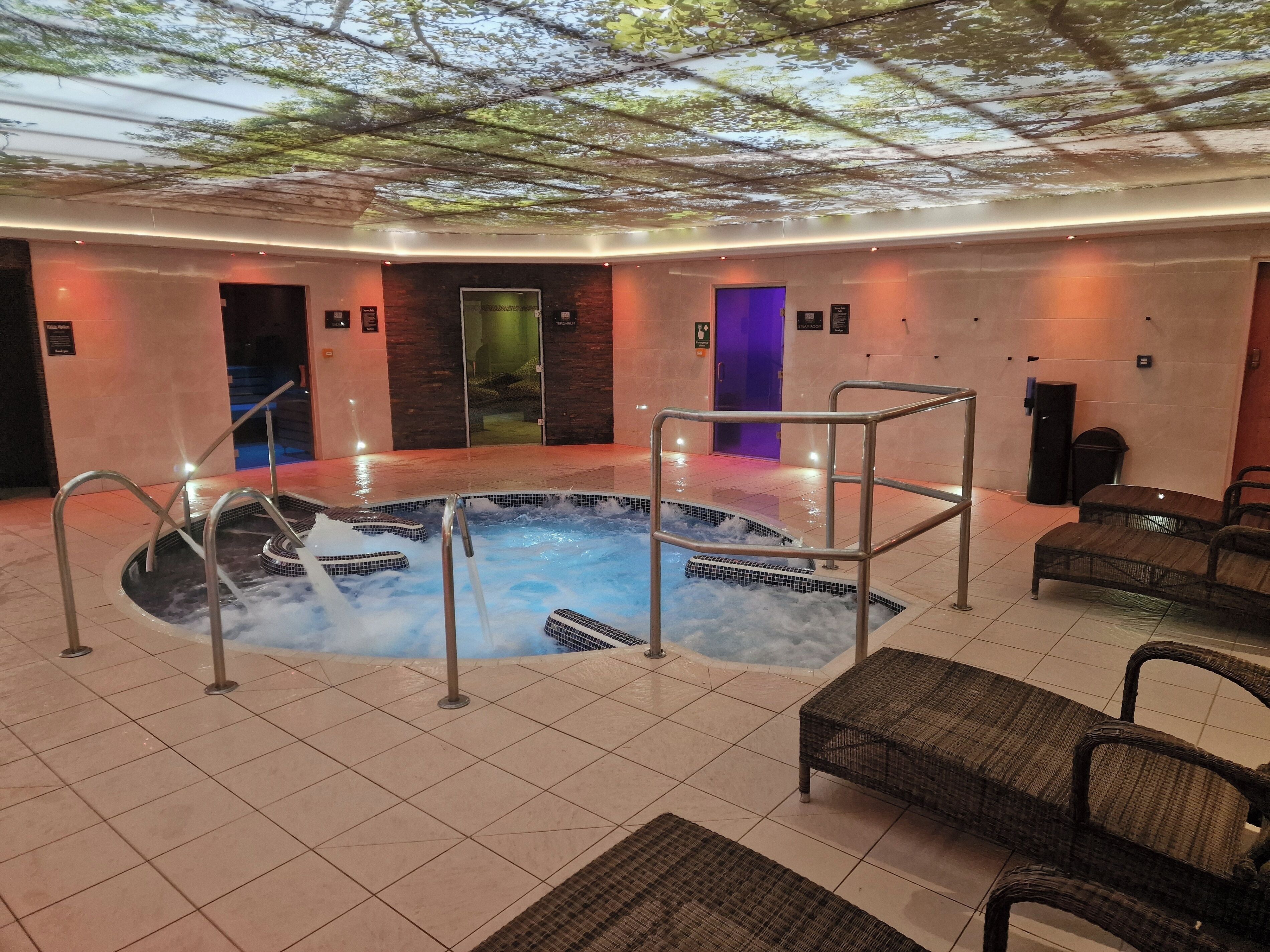 A hot tub area with tiled flooring, metal railings, and wicker furniture.