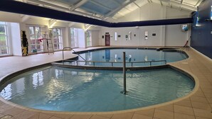 Una piscina interior con suelo de baldosas, una escalera metálica y un techo con tragaluces.