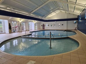 Ein Hallenbad mit gefliestem Boden, einer Metallleiter und einer Decke mit Dachfenstern.