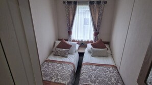 Una habitación pequeña con dos camas, una puerta y una ventana con cortinas.