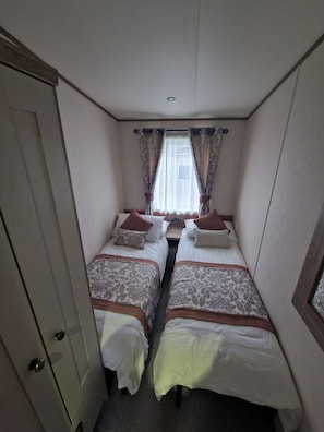 Ein schmales Zimmer mit zwei Betten, einer Tür und einem Fenster mit Vorhängen.
