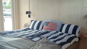 En säng med randigt sänglinne, en kudde med ett motiv av den amerikanska flaggan och en väggmonterad lampa.