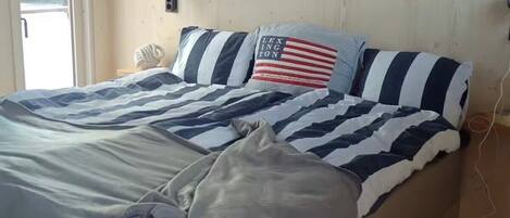 A bed with striped bedding, a pillow with an American flag design, and a wall-mounted light fixture.