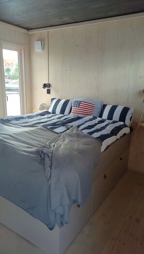Een bed met streepjesbeddengoed, een kussen met een ontwerp van de Amerikaanse vlag en een wandlamp.