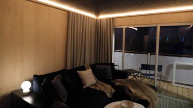 Ett rum med en soffa i mörk färg, ett litet bord med en kopp på och ett fönster med gardiner.