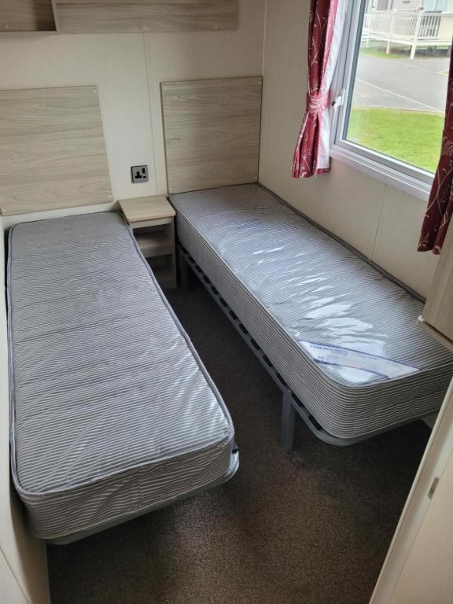 Habitación pequeña con dos camas individuales, una mesita y una ventana con cortinas.