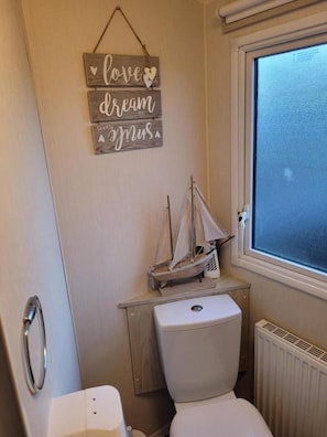 Un baño pequeño con un inodoro, un tocador de madera, un adorno náutico y un cartel con la inscripción 'love dream music' en la pared.