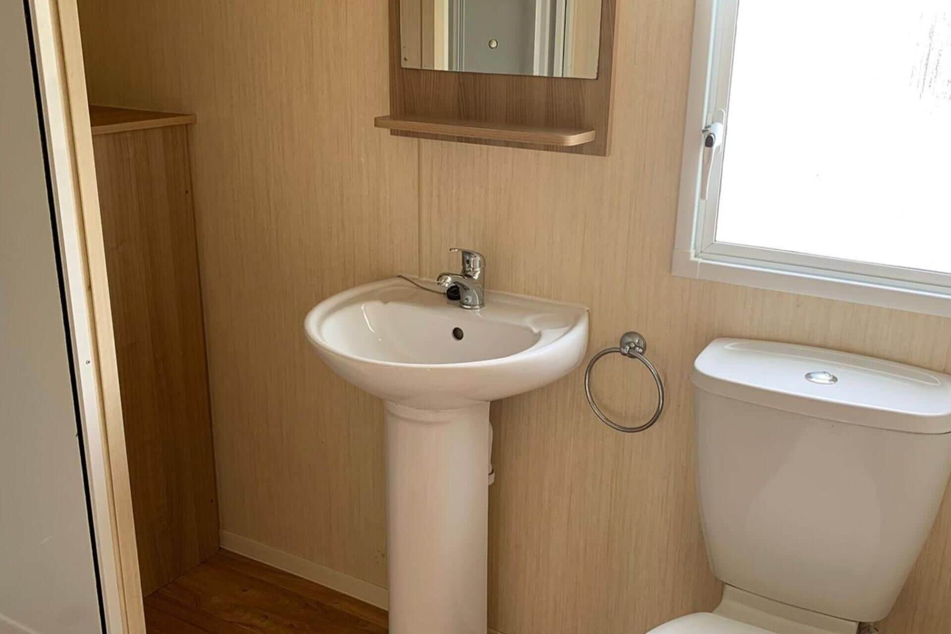 Ein Badezimmer mit einem Standwaschbecken, einer Toilette und einem Spiegel über dem Waschbecken.