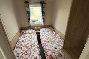 Habitació petita amb dos llits, una finestra amb cortines i una porta.