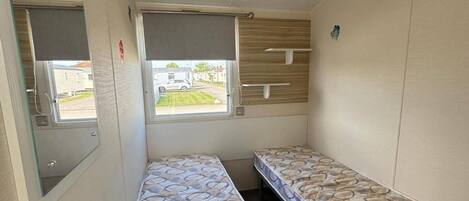 Quarto pequeno com duas camas de solteiro, janela com vista para uma casa e parede de painel de madeira.